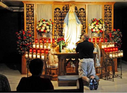 Catholic man kneels and prays in front of the Virgnin Mary
